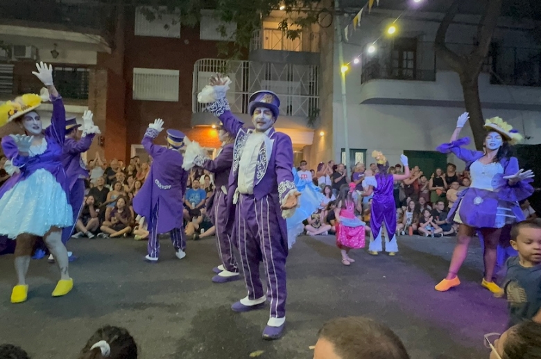 Murga performers wearing colorful purple, yellow, and blue costumes.